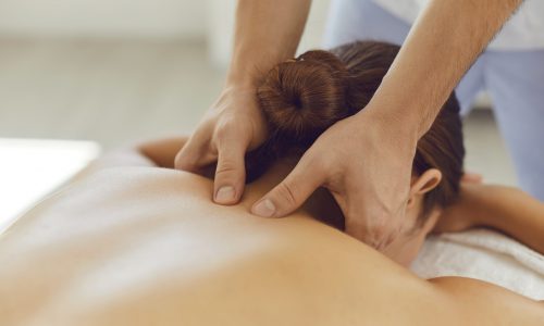 Close-up of woman lying on massage table face down enjoying spa procedures. Young female patient receiving professional remedial body massage in massage room of modern wellness center